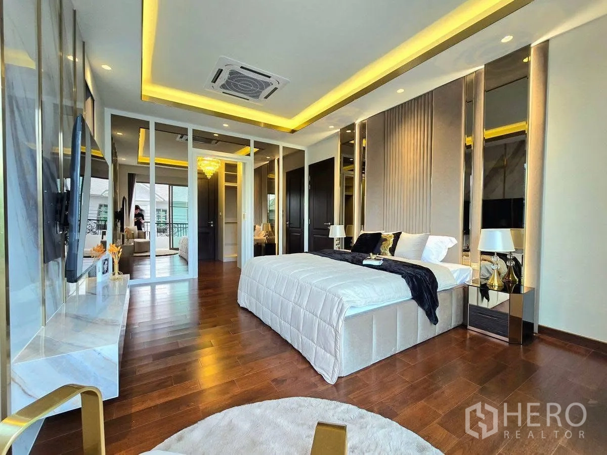 Detached House for rent or sale in Bang Phli, Samut Prakan - Large bedroom with TV feature wall, balcony doors, wood floors and gold-accent ceiling lights.