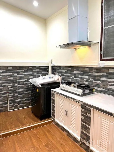 Townhouse for rent in Bang Na, Bangkok - Compact kitchen corner with range hood, gas cooktop, tile backsplash and utility space.