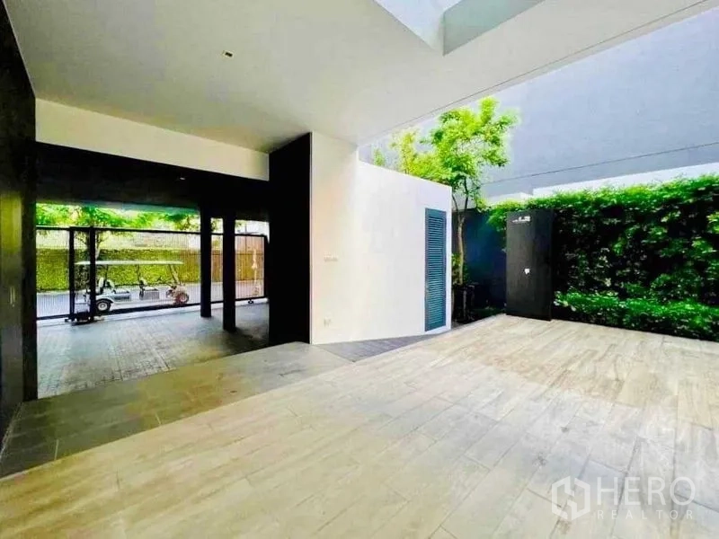 Detached House for sale in Huai Khwang, Bangkok - Covered patio and carport area with wood-look tiles and green hedges.