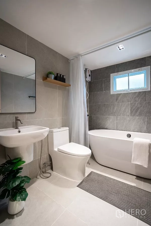 Detached House for rent in Huai Khwang, Bangkok - Stylish bathroom with bathtub, toilet, sink and gray wall tiles.