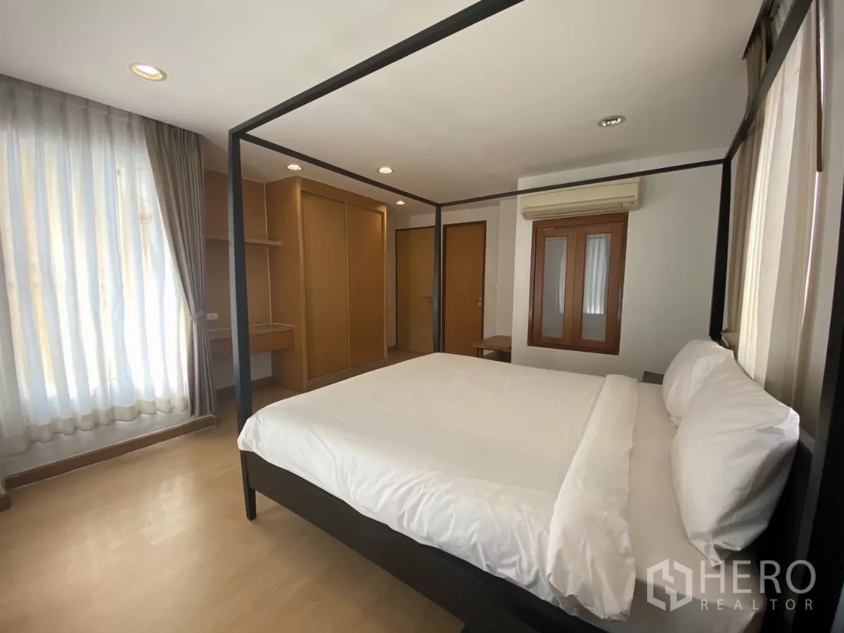 Condominium for rent in Watthana, Bangkok - Master bedroom with four-poster bed, built-in wardrobes and large windows with sheer curtains.