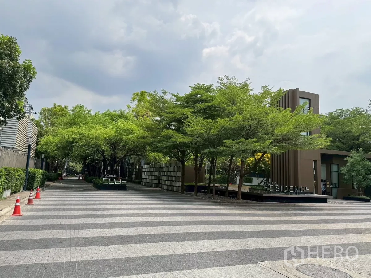 Townhouse for rent in Suan Luang, Bangkok - Tree-lined entrance of Noble Cube residence with project signage.