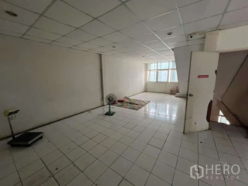 Shophouse for rent or sale in Khlong Toei, Bangkok - Empty tiled room with drop ceiling and window, suitable for office or storage.