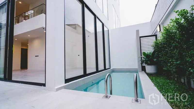 Townhouse for sale in Phra Khanong, Bangkok - Private narrow plunge pool beside floor-to-ceiling glass walls and a small lawn.
