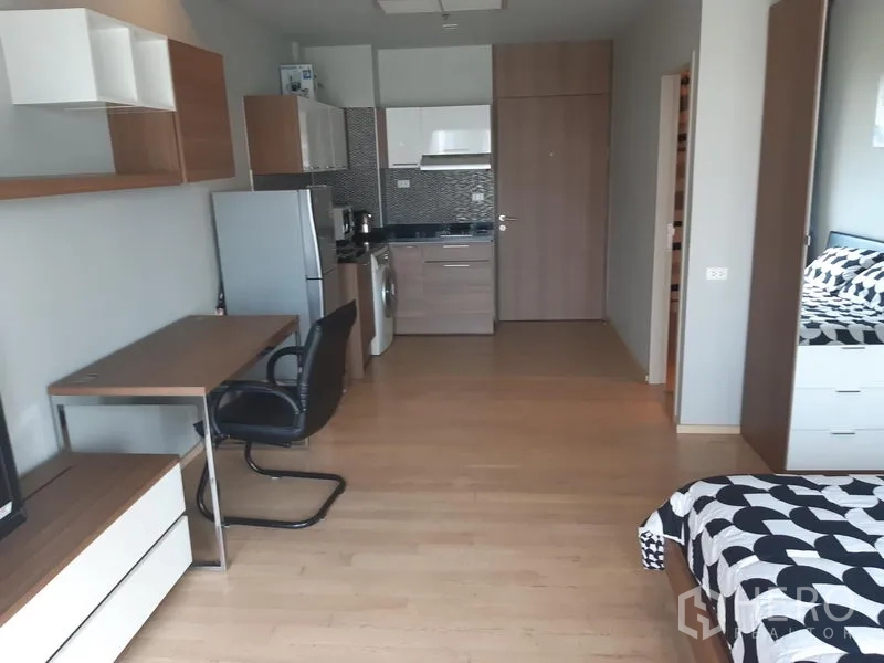 Condominium for rent in Bangkok - Open-plan living with work desk, TV cabinet, wall shelving, and a compact kitchen with fridge and washer.