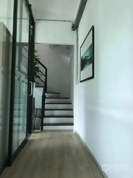 Shophouse for rent in Watthana, Bangkok - Hallway with glass wall and light wood floor leading to a staircase.