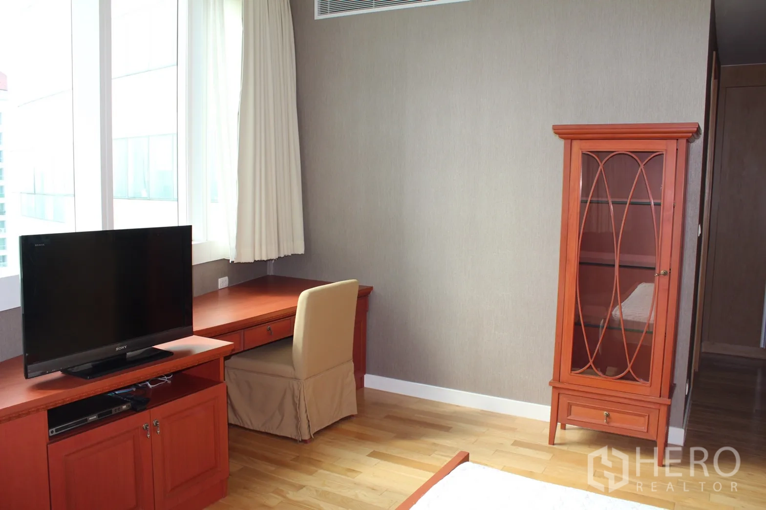 Condominium for rent in Khlong Toei, Bangkok - Bedroom corner with study desk by large window, flat-screen TV stand and glass display cabinet.