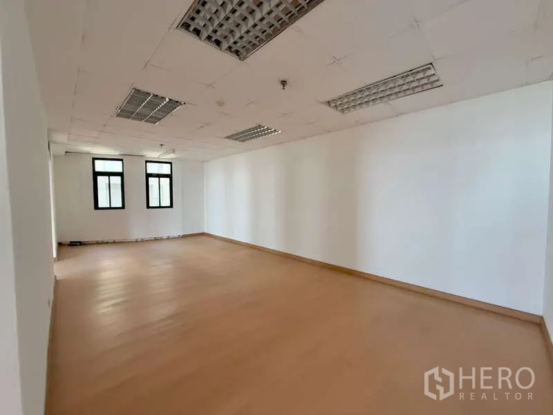 Office Space for rent in Chatuchak, Bangkok - Bright unfurnished office with wood-look floors, white walls and three black-framed windows.