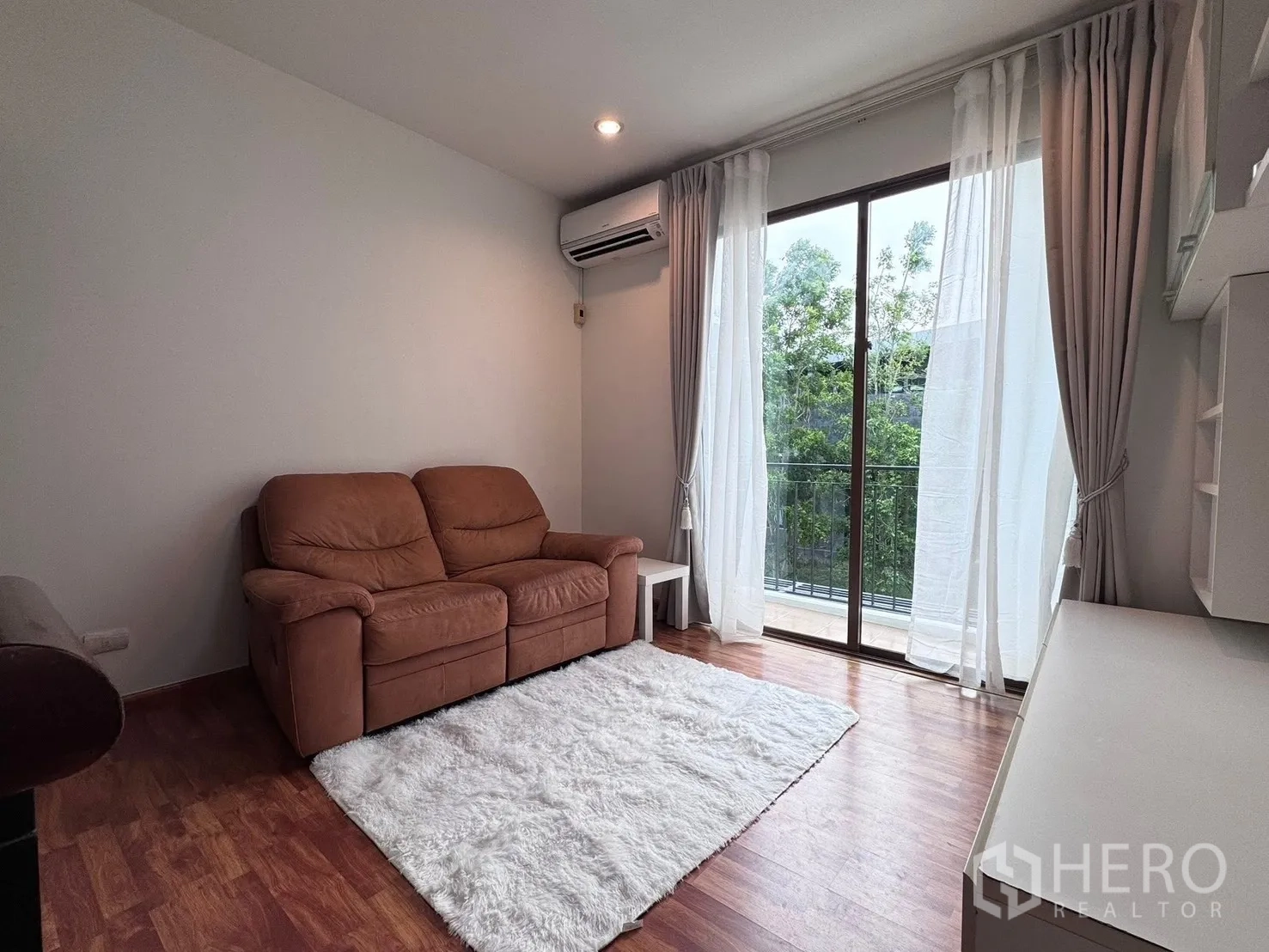 Townhouse for rent in Phra Khanong, Bangkok - Living room showing sofa, white rug, and sliding glass to balcony.