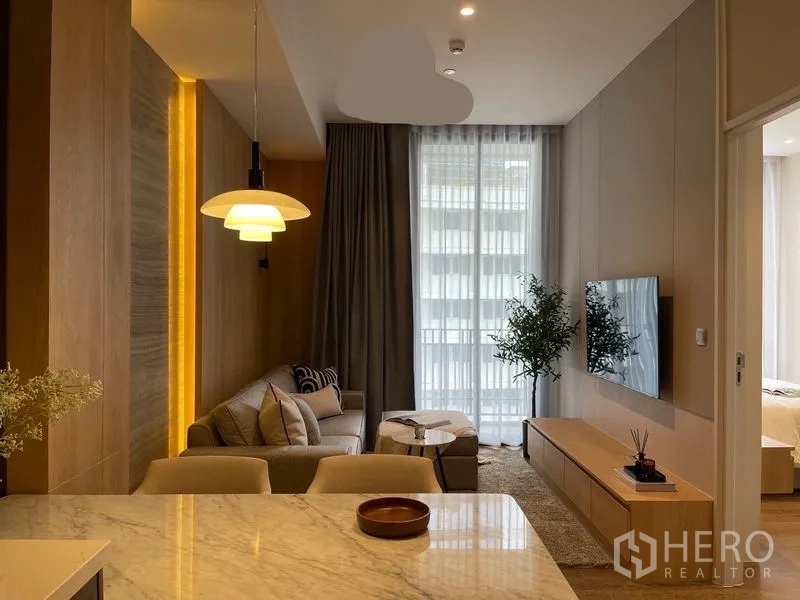 Condominium for rent or sale in Pathum Wan, Bangkok - View from kitchen toward living room with pendant lamp, floor-to-ceiling windows and bedroom entrance.