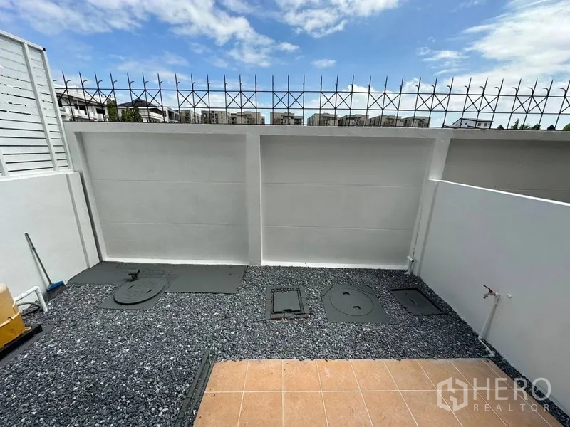 Townhouse for rent or sale in Phra Khanong, Bangkok - Private backyard utility area with gravel surface, high wall, and blue sky.