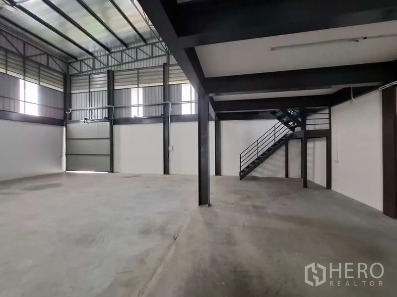 Warehouse for rent or sale in Bang Phli, Samut Prakan - Ground-level storage space with stairs to mezzanine and roller door.