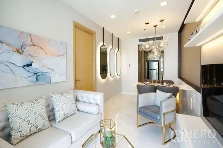 Condominium for rent in Watthana, Bangkok - Open-plan living and dining room with sofa and armchair, modern lighting, built-in shelving, and glossy floors.