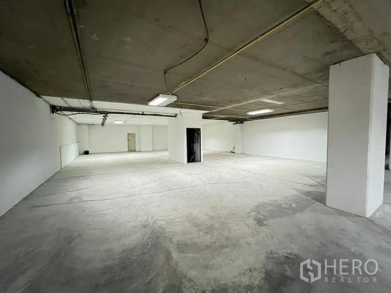 Office Space for rent - Wide raw office floor with columns, a doorway and cable runs on the ceiling.
