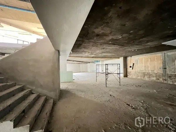 Retail Space for rent in Watthana, Bangkok - Spacious unfinished interior with internal staircase and scaffold, ideal for showroom layout.
