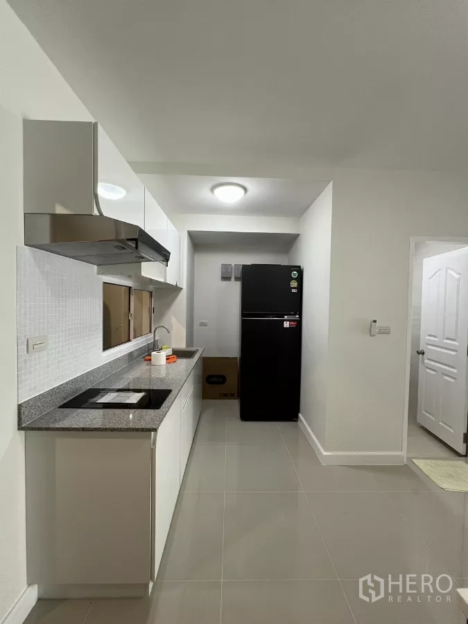 Townhouse for rent in Bang Kapi, Bangkok - Galley kitchen with granite countertop, hob and black refrigerator.