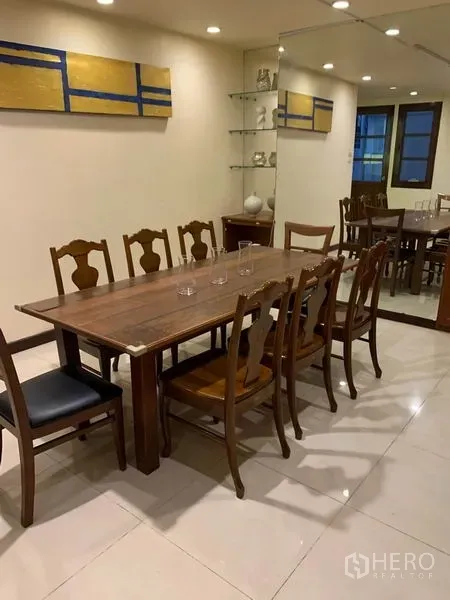 Townhouse for rent or sale in Phra Khanong, Bangkok - Long wooden dining table with chairs beside a mirrored wall and glass shelves.