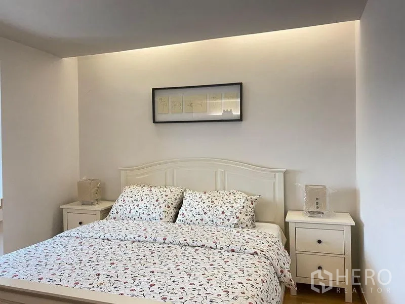 Condominium for sale in Phra Khanong, Bangkok - Master bedroom with white bedframe, floral bedding, twin nightstands, and cove lighting.