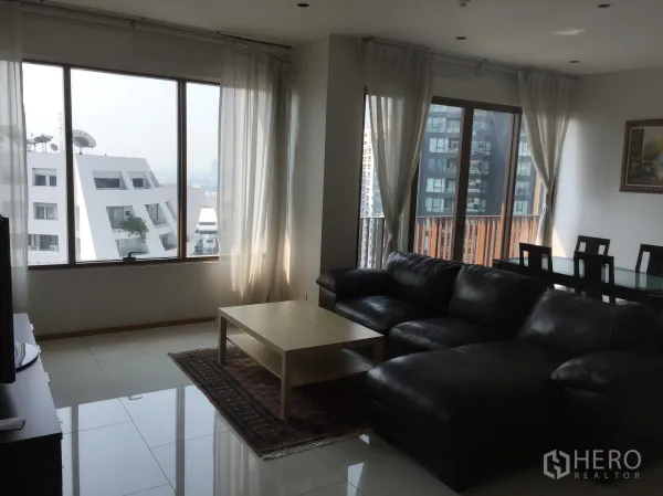 Condominium for rent or sale in Khlong Toei, Bangkok - Corner lounge with city view through wide windows and sheer curtains beside the dining area.