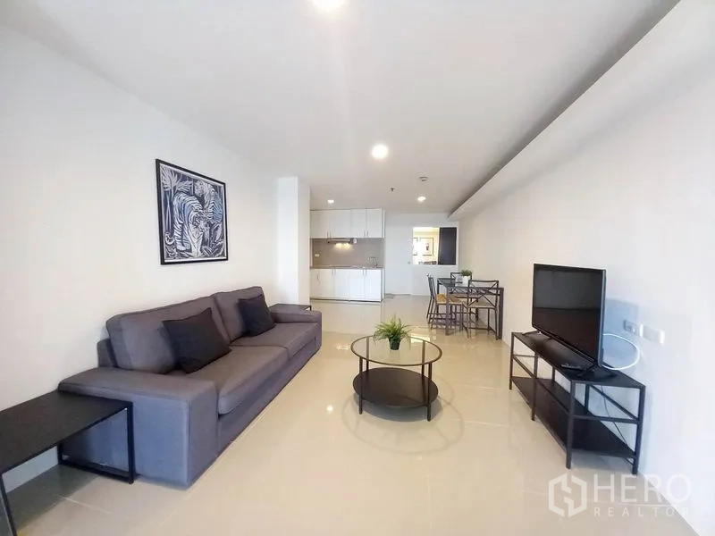 Condominium for rent in Khlong Toei, Bangkok - Open-plan living room with sofa, TV stand, round coffee table and kitchenette.