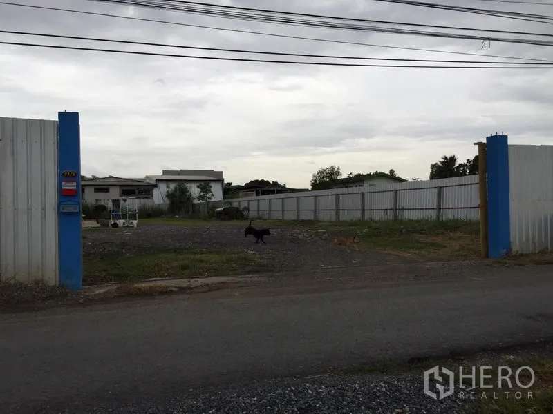 Warehouse for rent in Mueang Pathum Thani, Pathum Thani - Street-facing double gate leading into an expansive fenced compound with ample yard space.