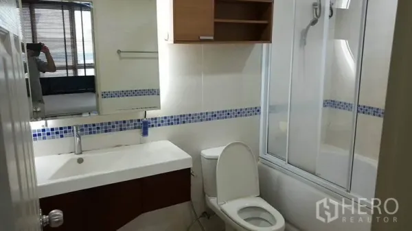 Condominium for rent in Bang Rak, Bangkok - Modern bathroom with wide vanity, toilet, bathtub with glass shower screen and blue mosaic tile accent.