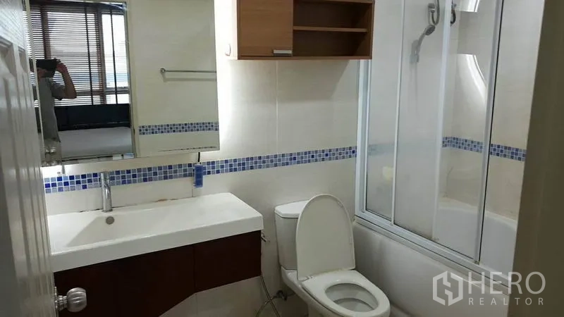Condominium for rent in Bang Rak, Bangkok - Modern bathroom with wide vanity, toilet, bathtub with glass shower screen and blue mosaic tile accent.