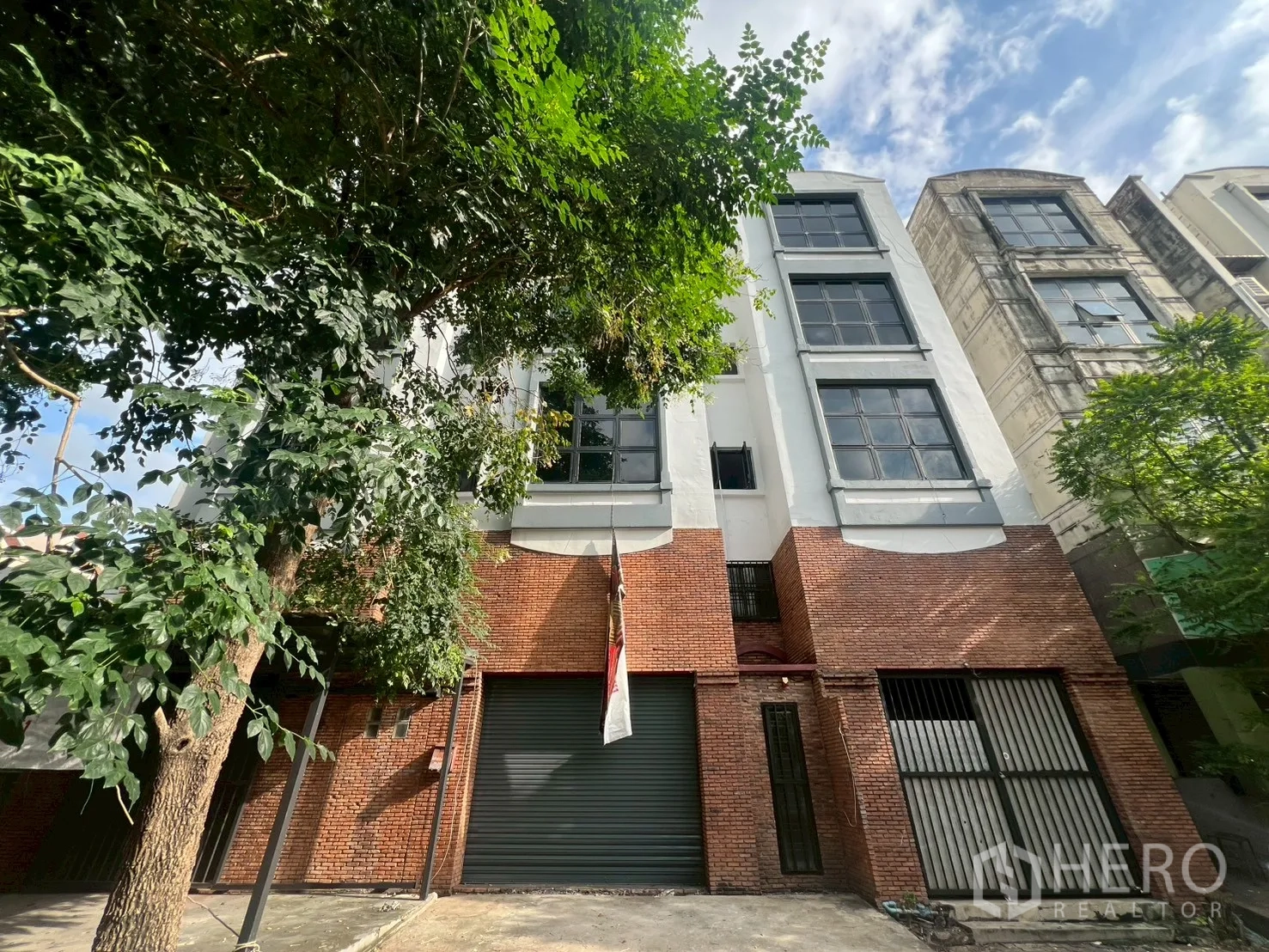 店屋 出租在Phra Khanong, Bangkok - 店屋正立面，宽卷闸门与栅栏入口，上层为白色外墙和大窗。