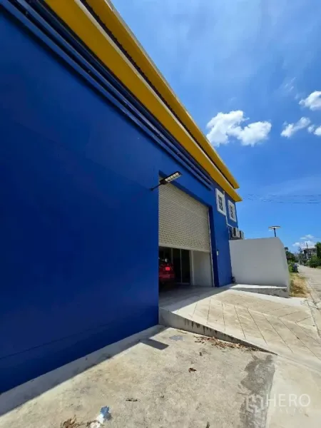 Warehouse for rent or sale in Khlong Toei, Bangkok - Front ramp and large roller shutter entrance of the warehouse with a car inside.