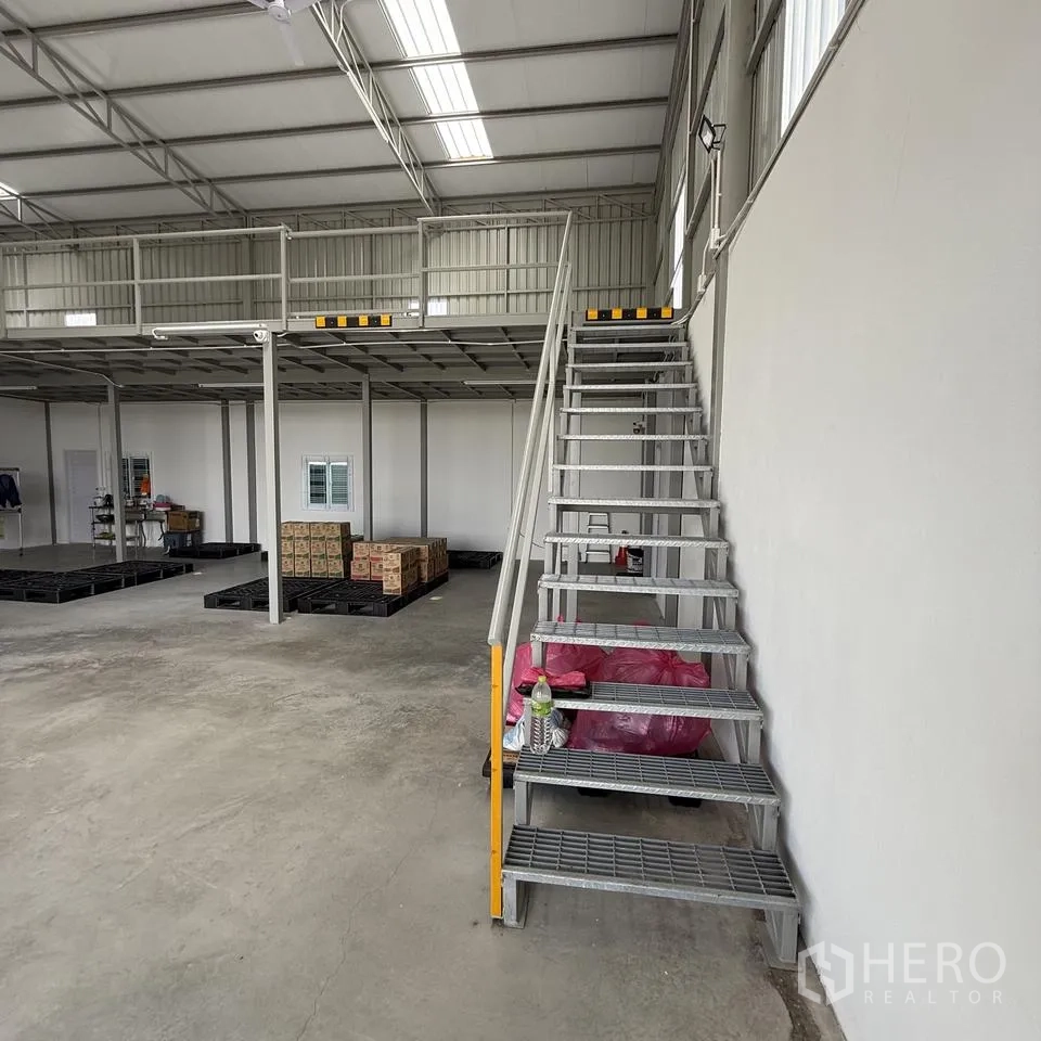 Warehouse for rent or sale in Khlong Luang, Pathum Thani - Warehouse interior with steel staircase to a mezzanine, concrete floor, pallets and boxes.