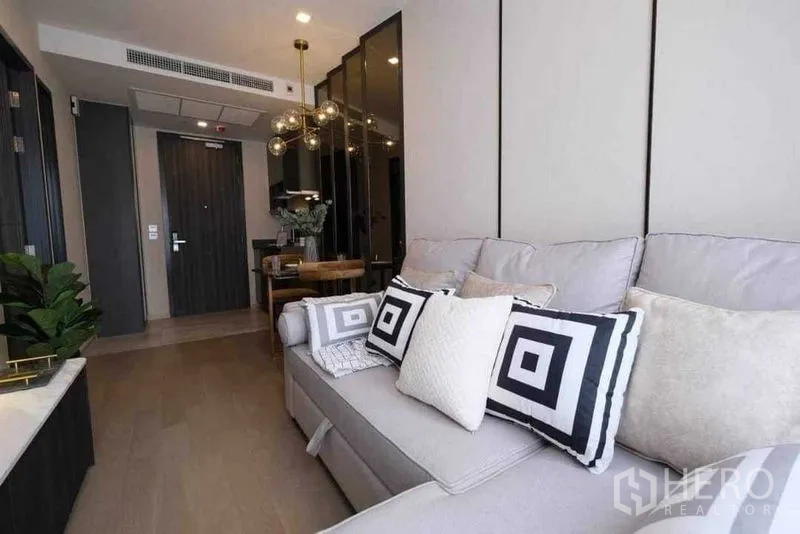 Condominium for rent in Watthana, Bangkok - Soft grey sofa with patterned cushions facing the entryway and dining nook.