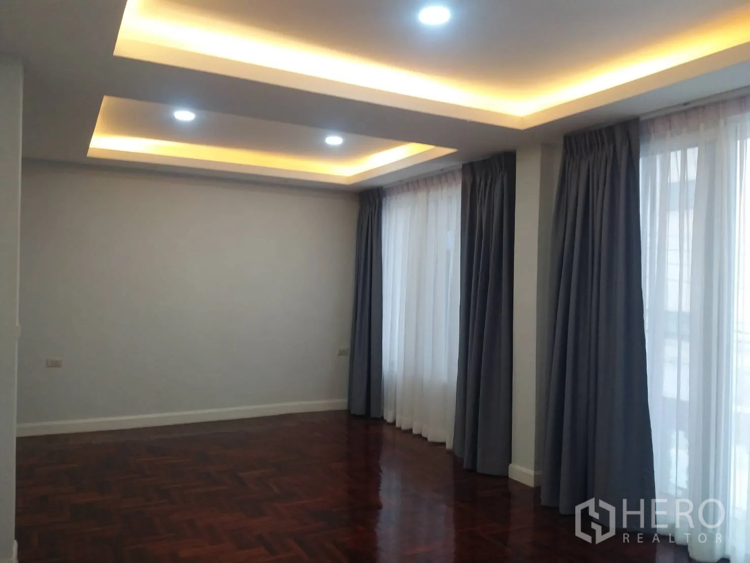 Townhouse for rent in Khlong Toei, Bangkok - Large corner bedroom featuring parquet floors, wide windows and layered ceiling lights.