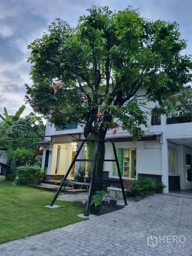 Detached House for rent in Bang Kapi, Bangkok - Two-storey detached house with large front lawn, mature tree, and paved driveway.