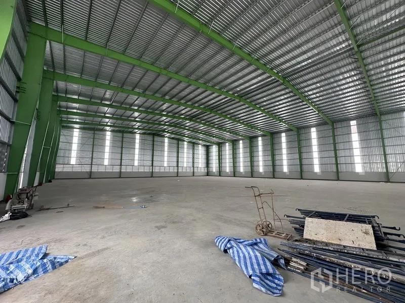 Warehouse for rent in Wang Noi, Phra Nakhon Si Ayutthaya - Warehouse hall with a cart and materials on the floor and tall windows for natural light.
