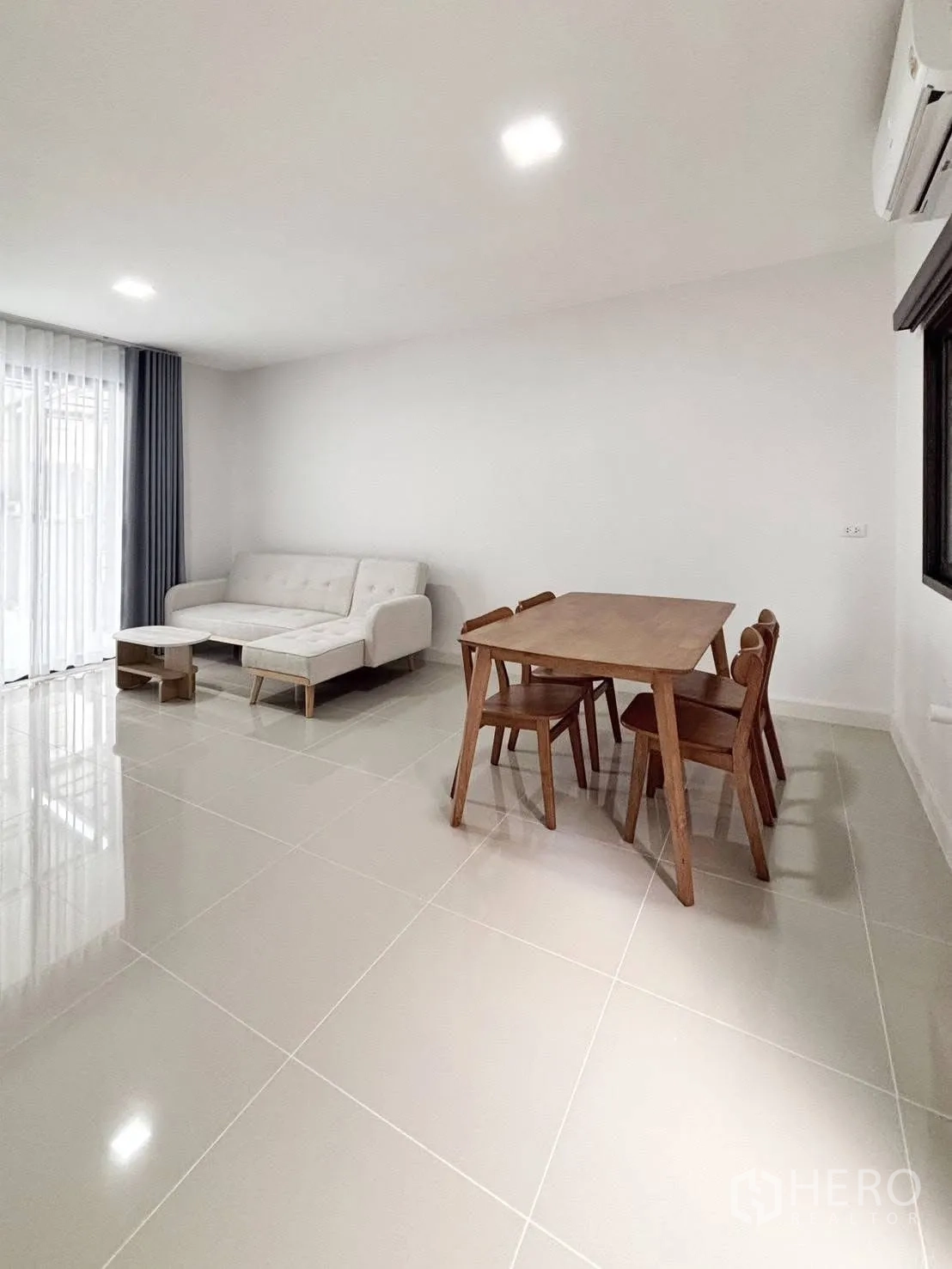 Townhouse for rent in Bang Phli, Samut Prakan - Open-plan living and dining area with glossy floor tiles, white sofa, dining set and sliding glass doors.