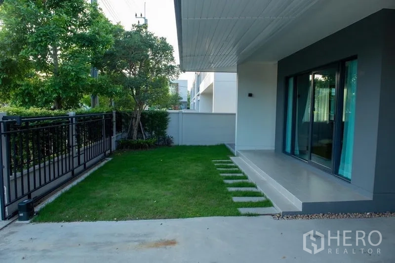 Detached House for rent in Bang Phli, Samut Prakan - Front lawn and patio beside sliding doors, bordered by a metal fence.