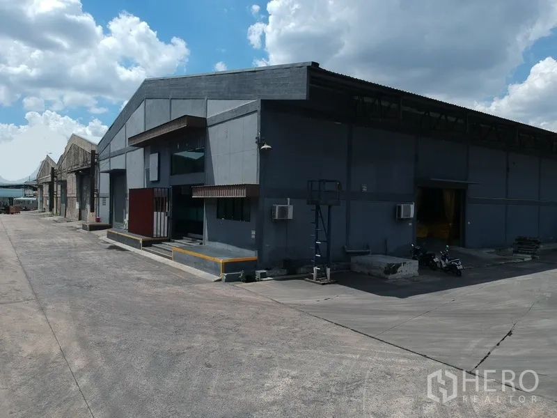 Factory for rent in Phra Pradaeng, Samut Prakan - Corner view of expansive warehouse row with multiple bays and a spacious concrete yard for logistics.