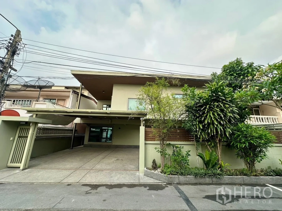 Detached House for rent in Watthana, Bangkok - Street view of the detached house facade with gated driveway and landscaped greenery.