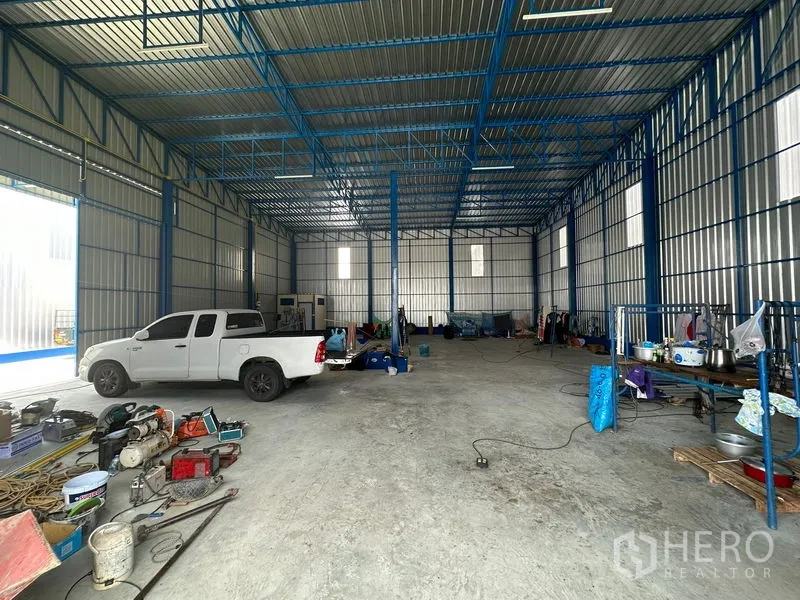 Warehouse for rent in Wang Thonglang, Bangkok - Spacious warehouse interior with blue truss ceiling, concrete floor, wide roller-door opening and parking space for a pickup.