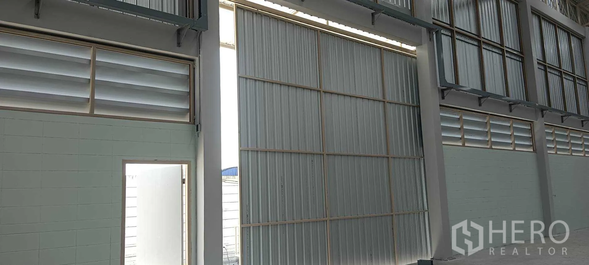 Warehouse for rent or sale in Lam Luk Ka, Pathum Thani - Large sliding metal door and louvered vents along the warehouse wall.