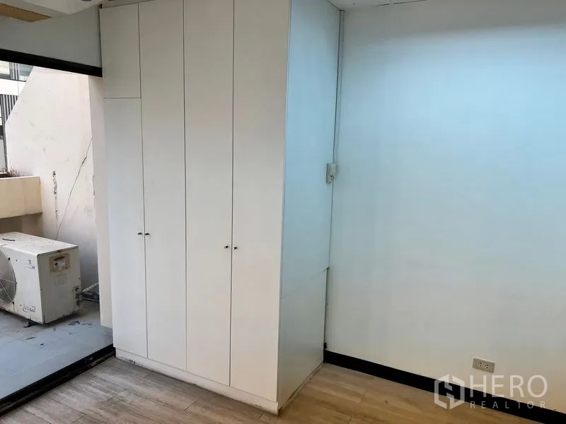 Office Space for rent in Pathum Wan, Bangkok - Built-in white storage cabinet beside a sliding door to a small balcony with AC compressor.