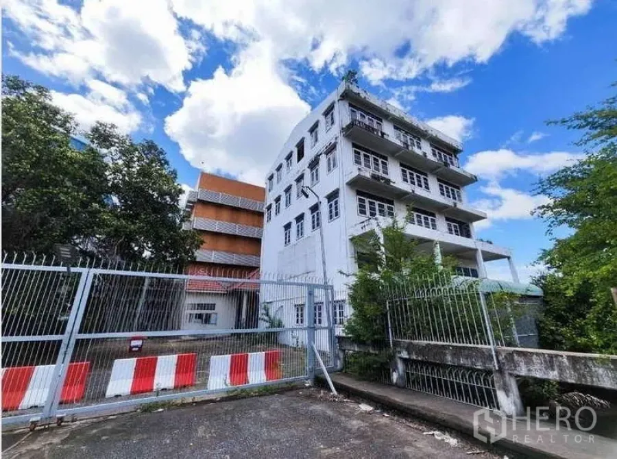 工厂 出租在Phra Samut Chedi, Samut Prakan - 带大门入口的独立工业园区，旁有多层办公楼和蓝天白云。