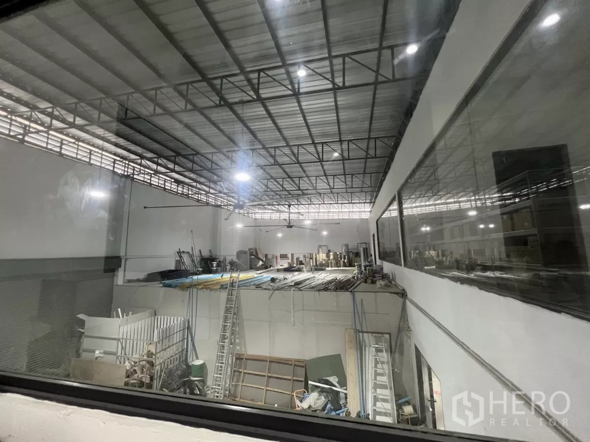 Warehouse for rent or sale in Lat Krabang, Bangkok - View through glass over the warehouse floor showing roof trusses and equipment.