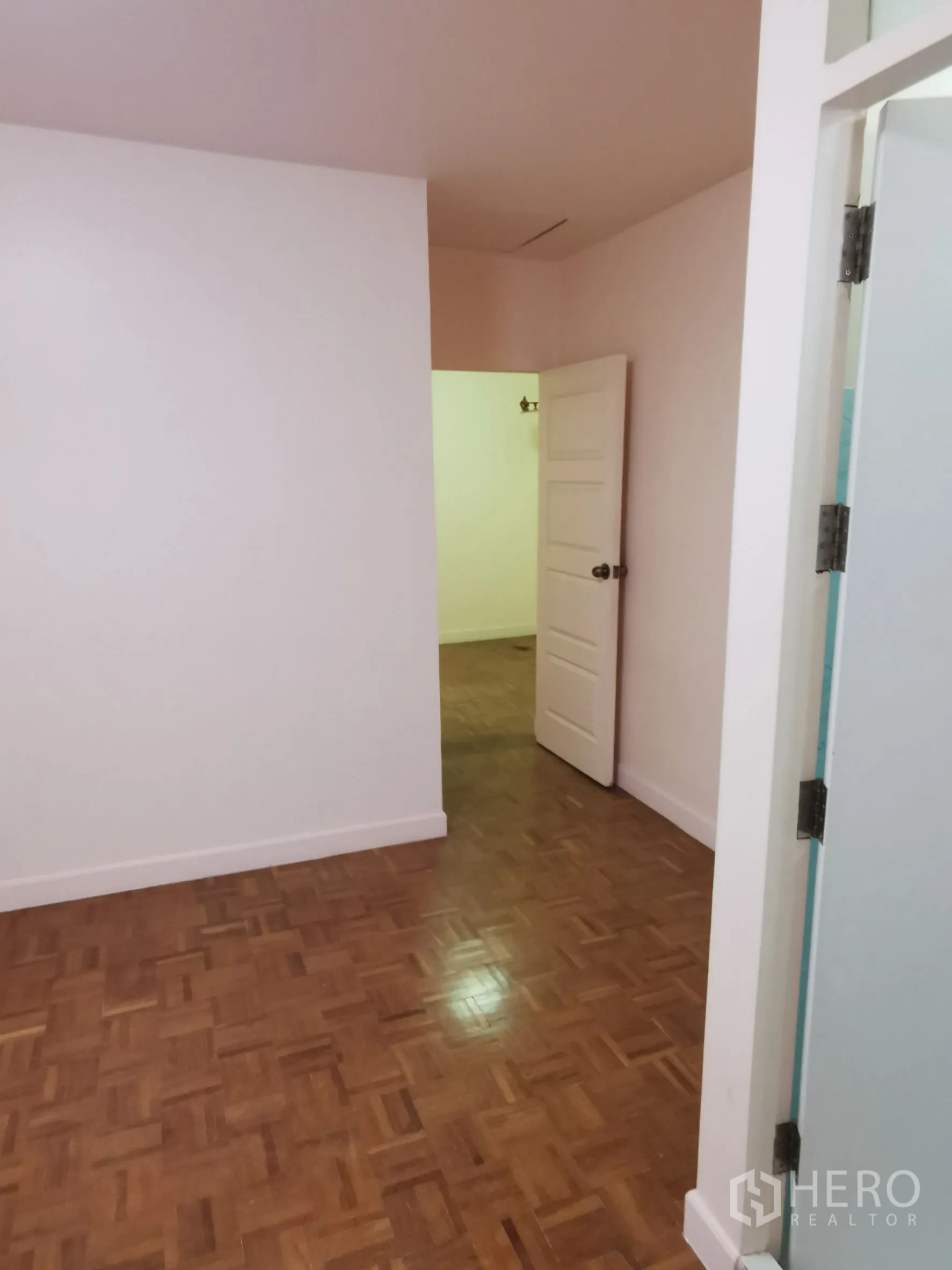 Townhouse for rent in Khlong Toei, Bangkok - Empty room with parquet flooring, soft pink walls, and an open door.