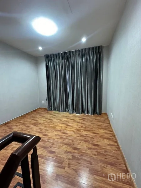 Townhouse for rent or sale in Phra Khanong, Bangkok - Cozy room with wood floors and dark drapes beside the stair hall.