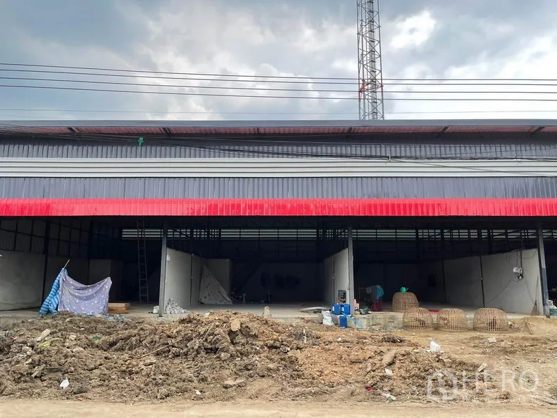 Warehouse for rent in Pathum Thani - Street-facing exterior of a metal-clad warehouse with wide open bays and a dirt work area in front.