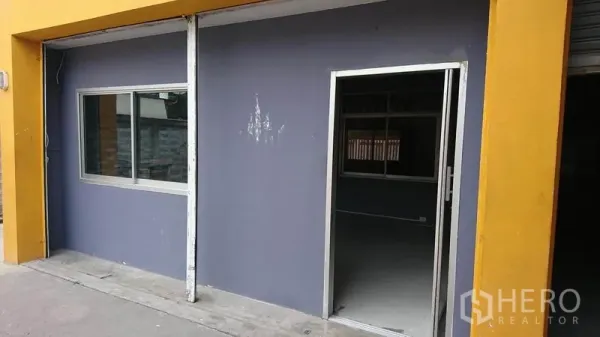Warehouse for rent in Lak Si, Bangkok - Front office entrance featuring a glass door and window set in a yellow-framed facade.