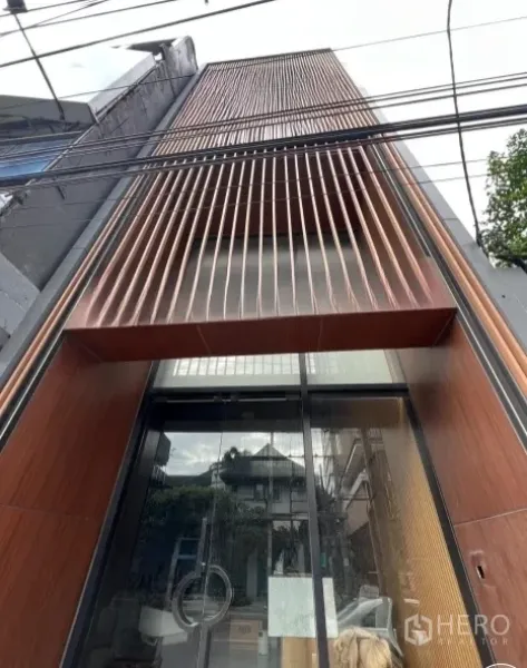 店屋 出租在Watthana, Bangkok - 现代商铺立面，竖向木格栅与全高玻璃入口，位于曼谷Ekkamai。