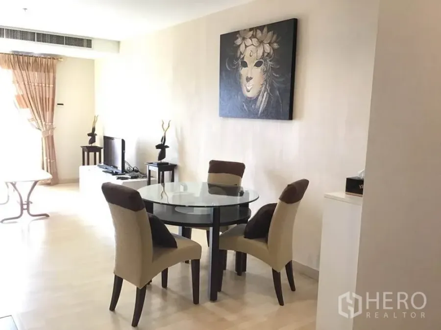 Condominium for rent in Watthana, Bangkok - Bright dining area with a round glass table, four upholstered chairs, light wood flooring, wall art, and a TV console by the window.