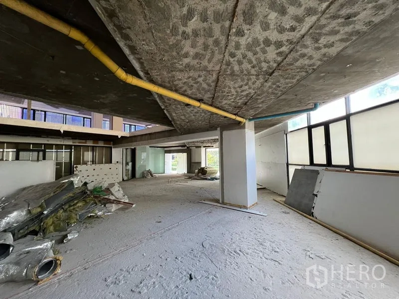 Retail Space for rent in Watthana, Bangkok - Open shell space with exposed piping, large windows and construction materials on the floor.